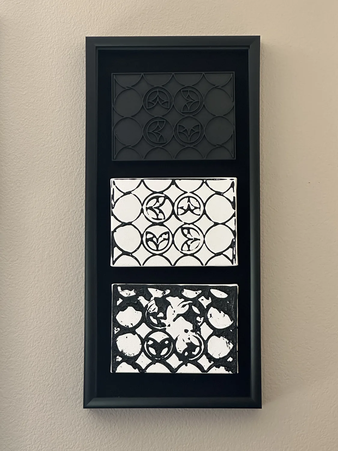 The finished piece hung on a wall in a tall black frame: the 3D-printed stamp at the top, the clean print below it, and the over-inked print at the bottom